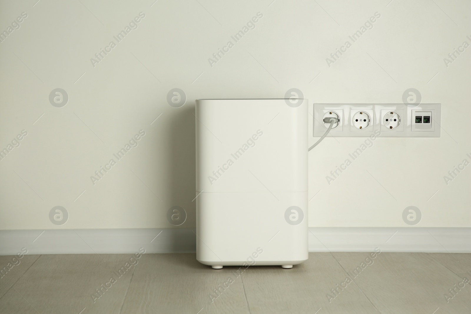 Photo of Modern air humidifier plugged into power socket on floor indoors