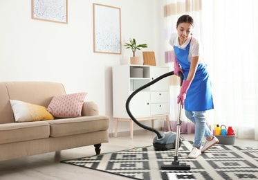 Photo of Woman hoovering carpet in living room. Cleaning service