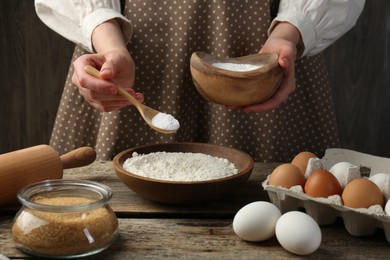 Photo of Making dough. Woman adding baking powder to flour at wooden table, closeup