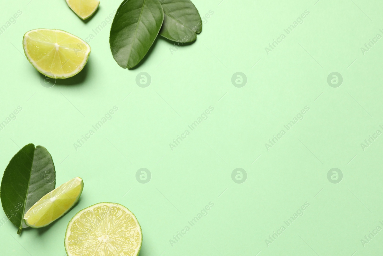 Photo of Cut fresh ripe limes with leaves on light green background, flat lay