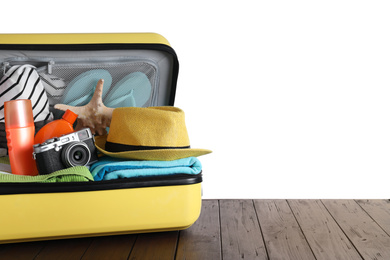 Open suitcase with different beach objects on wooden table against white background. Space for text