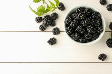 Bowl and fresh ripe blackberries on white wooden table, flat lay. Space for text