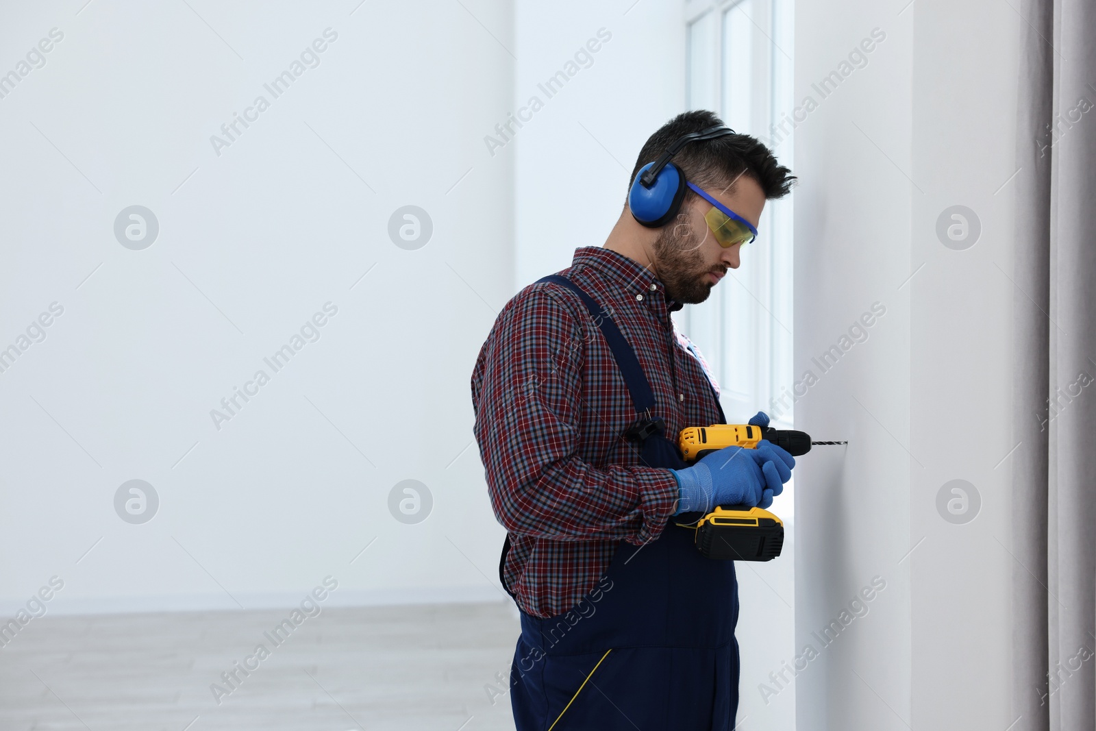 Photo of Young worker in uniform using electric drill indoors, space for text