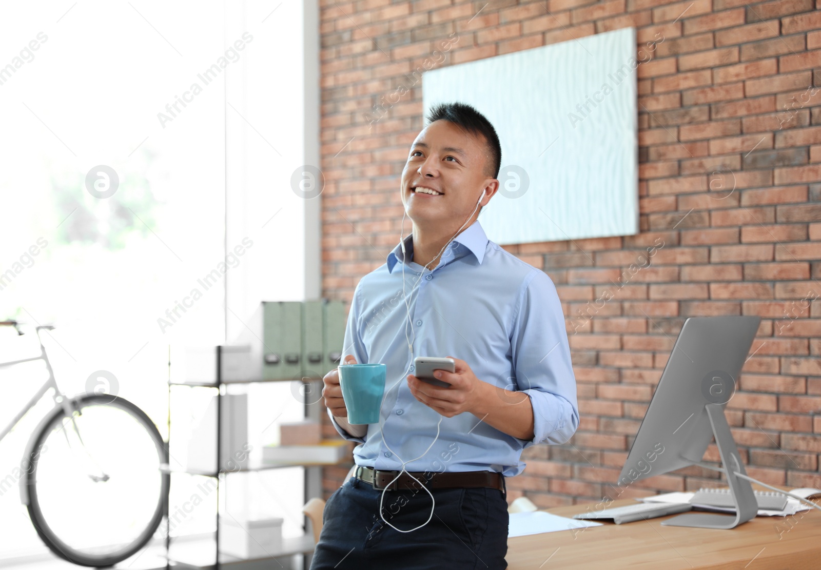 Photo of Happy young businessman with mobile phone listening to music in office. Peaceful moment