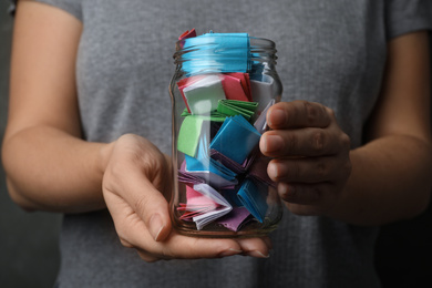Photo of Woman holding glass jar with colorful paper pieces, closeup on hands