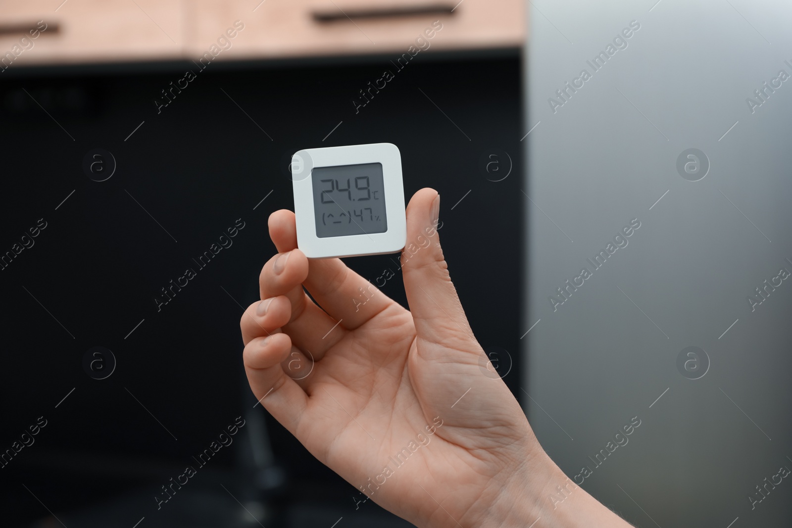 Photo of Woman holding digital hygrometer with thermometer at home, closeup