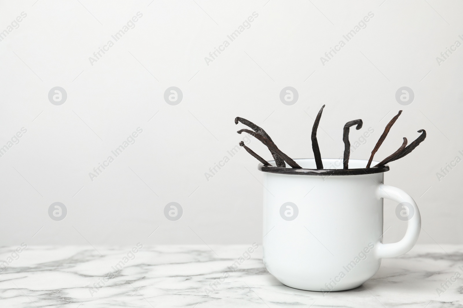 Photo of Mug with aromatic vanilla sticks on light background