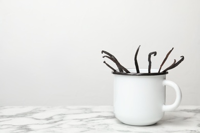 Photo of Mug with aromatic vanilla sticks on light background