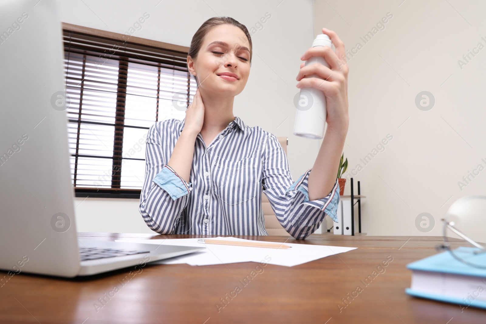 Photo of Young woman applying thermal water on face in office. Cosmetic product