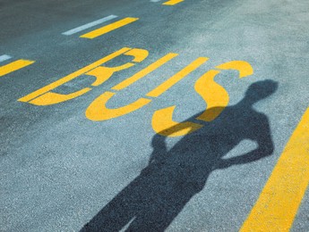 Photo of Bus stop pad and man's shadow on asphalt road