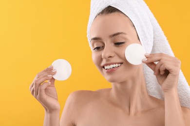 Photo of Removing makeup. Smiling woman with cotton pads on yellow background