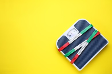 Scales and measuring tape on yellow background, top view. Space for text