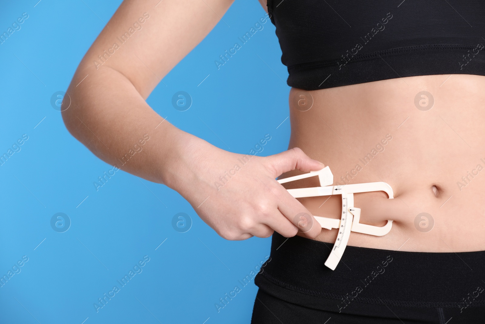 Photo of Young woman measuring body fat with caliper on blue background, closeup. Nutritionist's tool