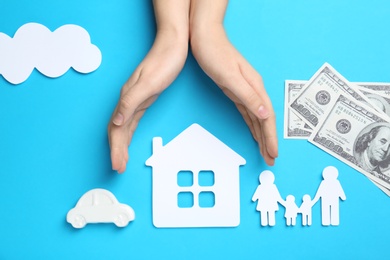 Woman holding hands over paper silhouettes of family, house and car on color background, top view. Life insurance concept