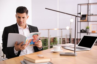 Photo of Man reading magazine at table in office