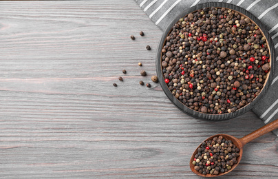 Different peppercorns on light grey wooden table, flat lay. Space for text