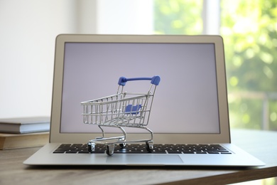 Photo of Internet shopping. Laptop with small cart on table indoors