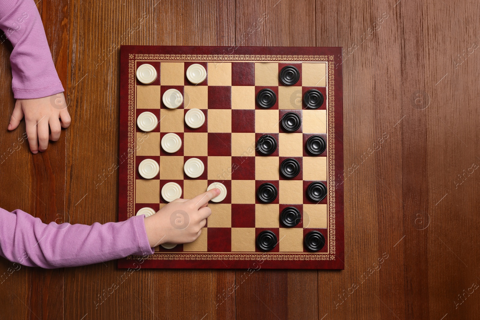 Photo of Playing checkers. Child thinking about next move at wooden table, top view