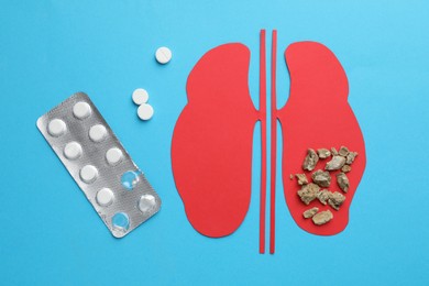 Paper cutout of kidneys with stones and pills on light blue background, flat lay
