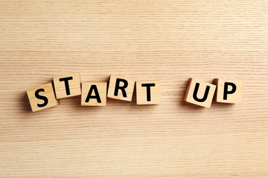 Words START UP made with cubes on wooden background, flat lay