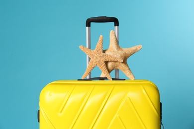 Stylish suitcase with sea stars on color background