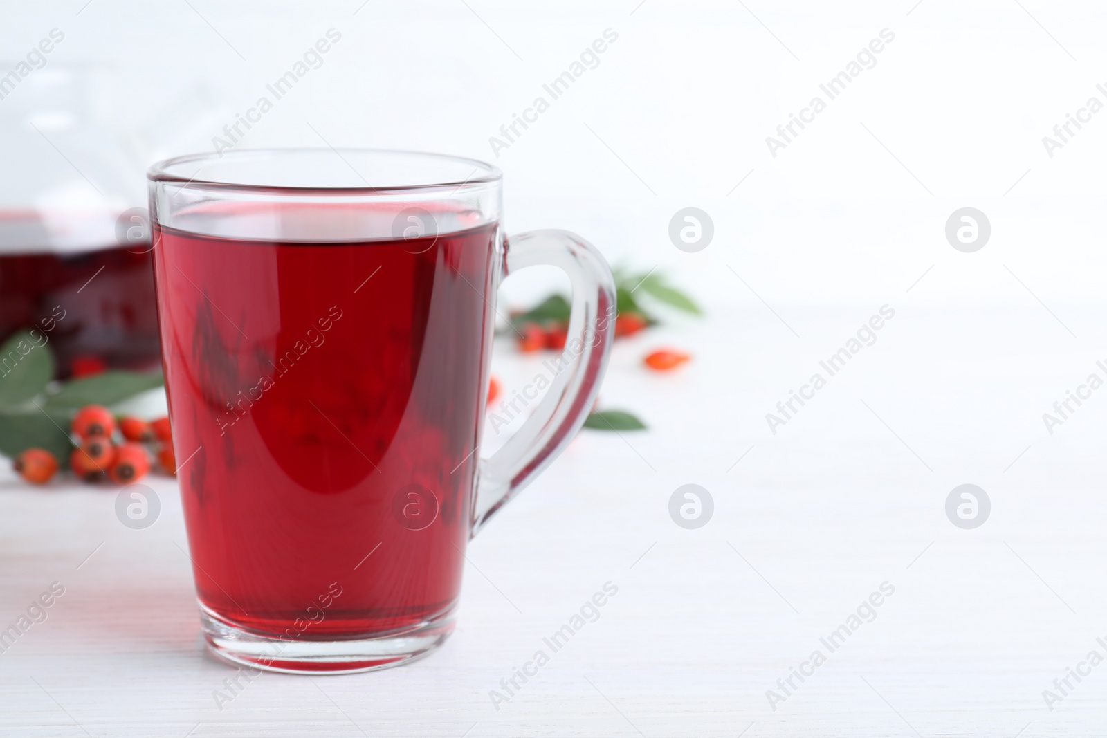 Photo of Aromatic rose hip tea and fresh berries on white wooden table, space for text