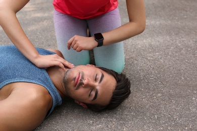 Young woman checking pulse of unconscious man on street