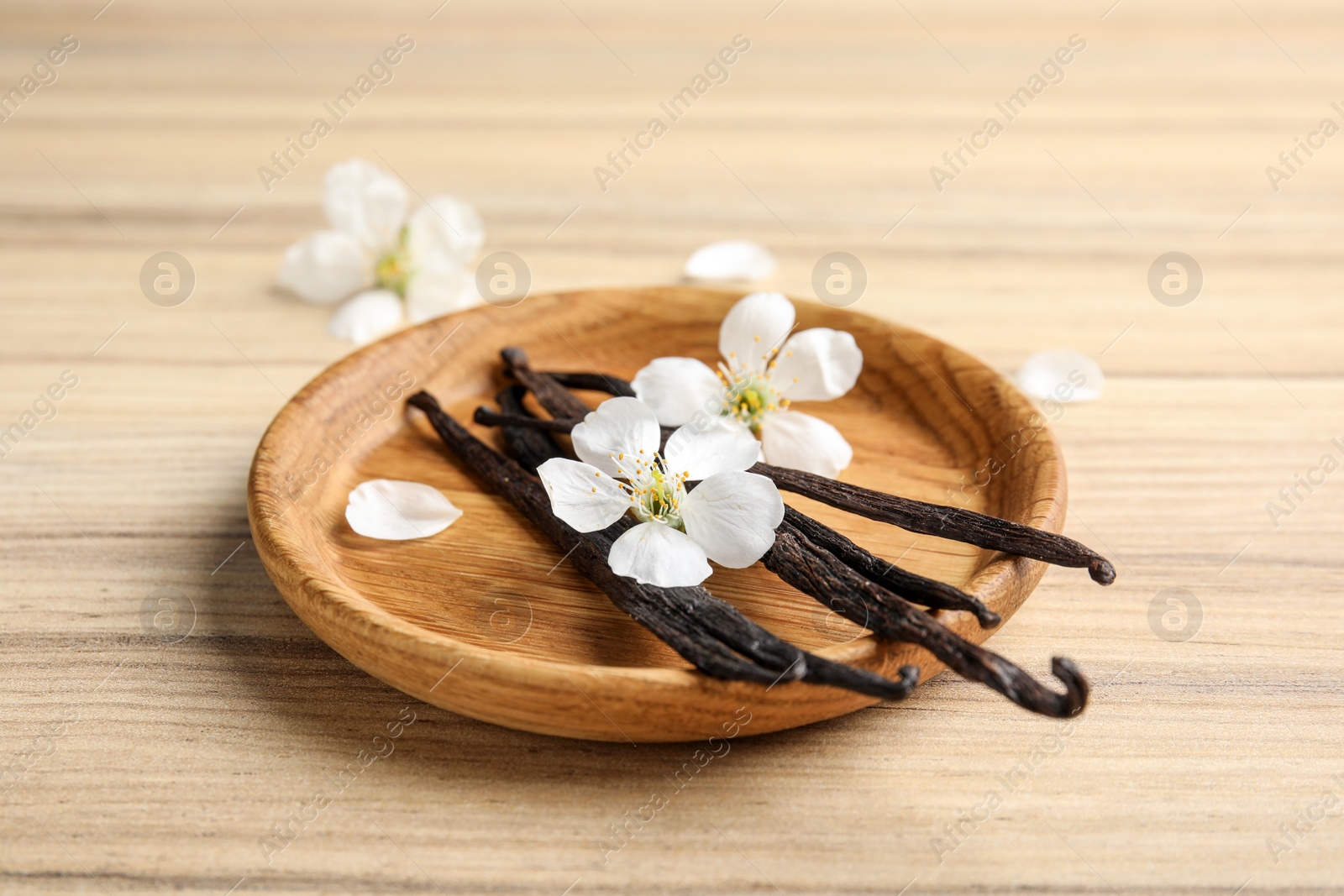 Photo of Plate with aromatic vanilla sticks and flowers on wooden background