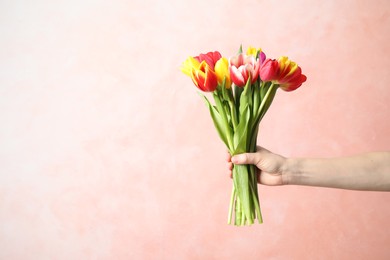 Photo of Woman holding beautiful spring tulips on light pink background, closeup. Space for text
