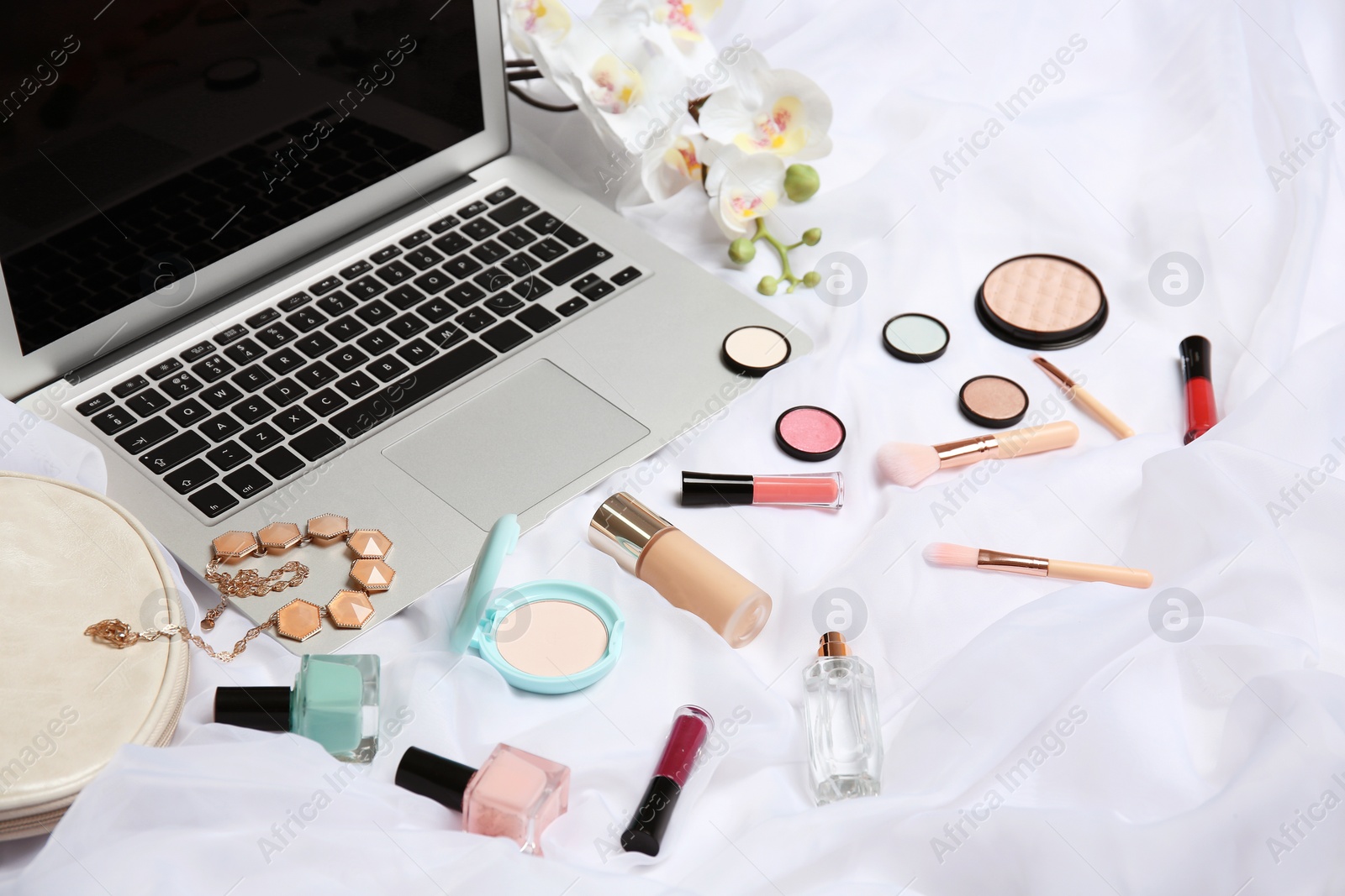 Photo of Composition with laptop and makeup products for woman on bed