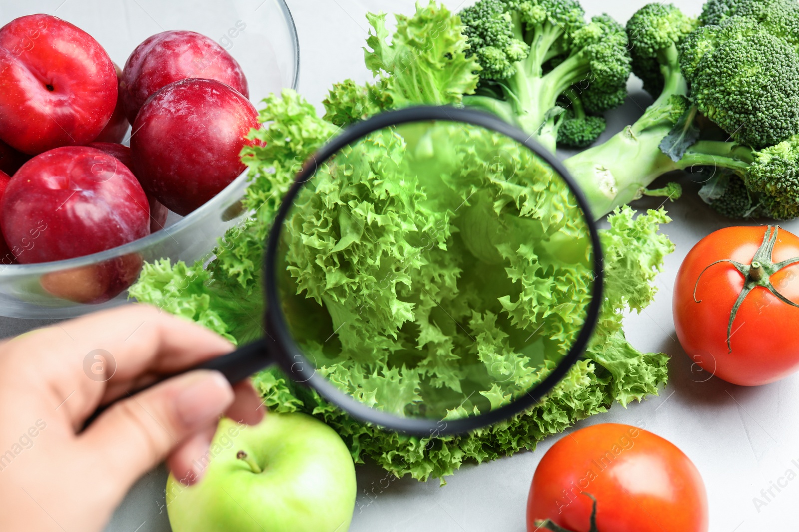 Photo of Woman with magnifying glass exploring vegetables and fruits, closeup. Poison detection