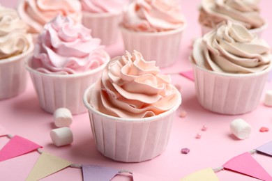 Photo of Delicious birthday cupcakes, bunting flags, marshmallows and sprinkles on pink background, closeup