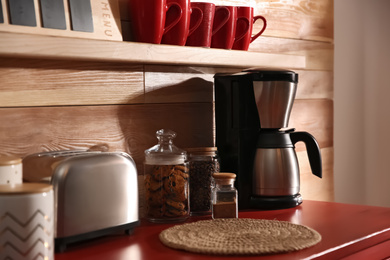 Photo of Modern coffeemaker and toaster on red table near wooden wall