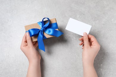 Photo of Woman holding gift box and blank card at light grey table, top view. Space for text