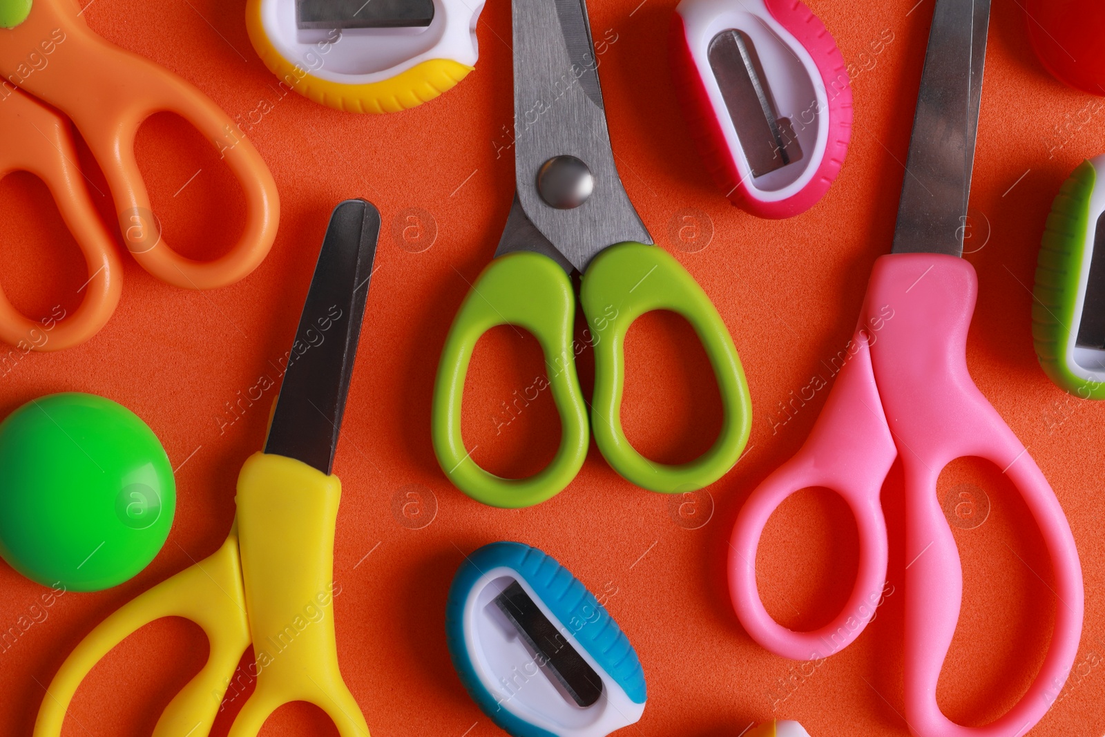 Photo of Different colorful scissors and sharpeners on orange background, flat lay