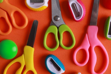 Photo of Different colorful scissors and sharpeners on orange background, flat lay