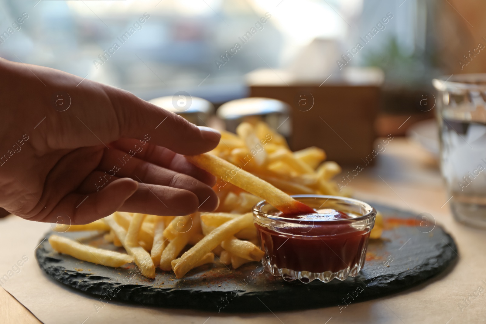 Photo of Woman dipping French fries into red sauce in cafe, closeup