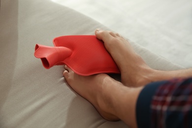 Man warming feet with hot water bottle on sofa, closeup