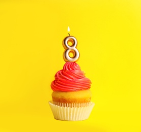 Photo of Birthday cupcake with number eight candle on yellow background