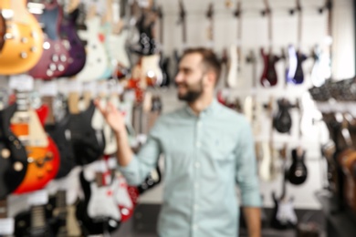 Photo of Young shop assistant near guitars in music store, blurred view