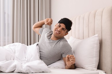Photo of Happy man awakening with sleeping mask in bed at home
