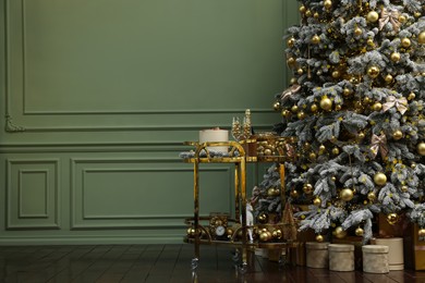 Beautiful Christmas tree, gift boxes, table and festive decor near olive wall indoors with space for text. Interior design