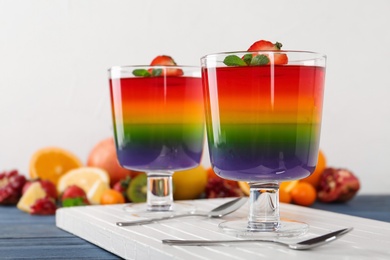 Photo of Dessert bowls of layered jelly served on blue wooden table against light background