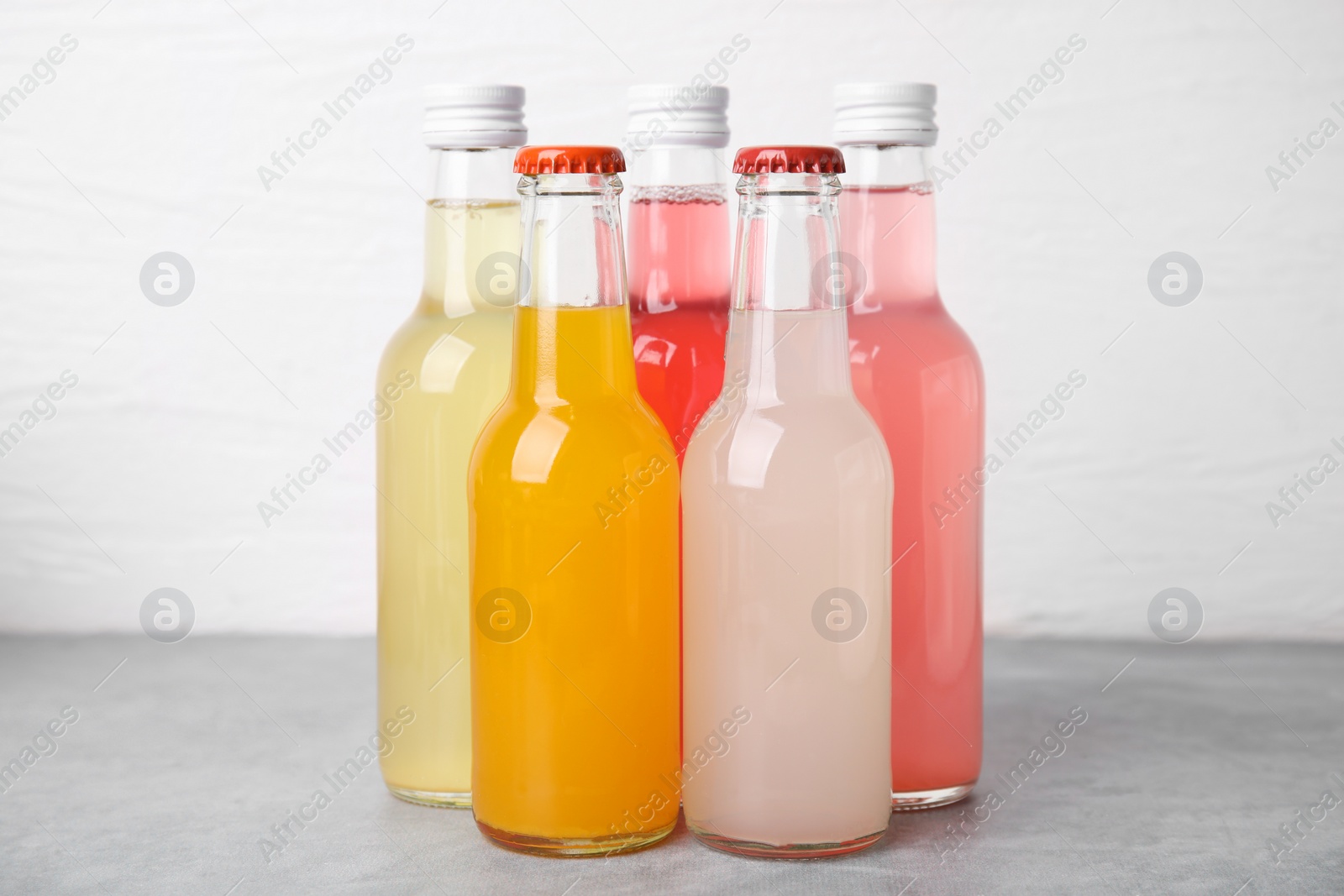 Photo of Delicious kombucha in glass bottles on grey table against white background