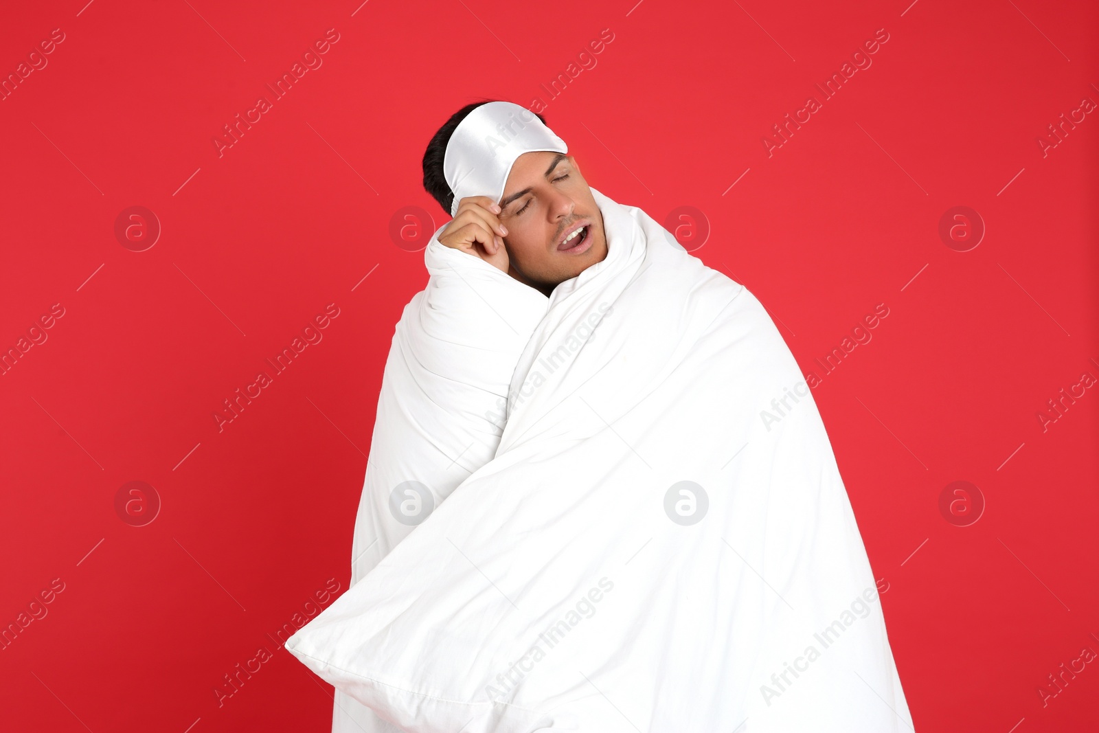 Photo of Man wrapped in blanket yawning on red background