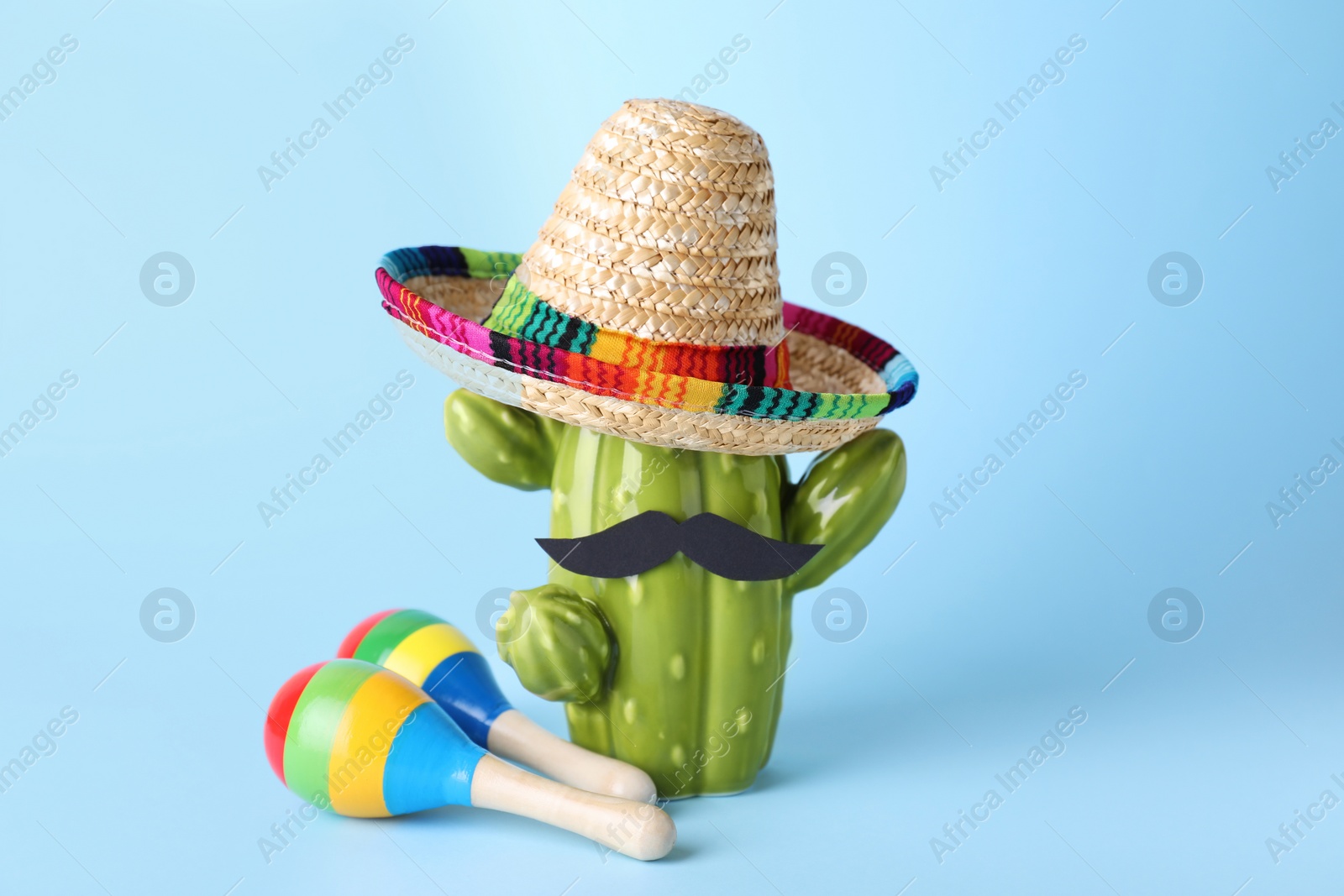 Photo of Colorful maracas, toy cactus with sombrero hat and mustache on light blue background. Musical instrument