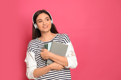 Photo of Young woman listening to audiobook on pink background. Space for text