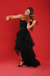 Photo of Beautiful woman playing violin on red background