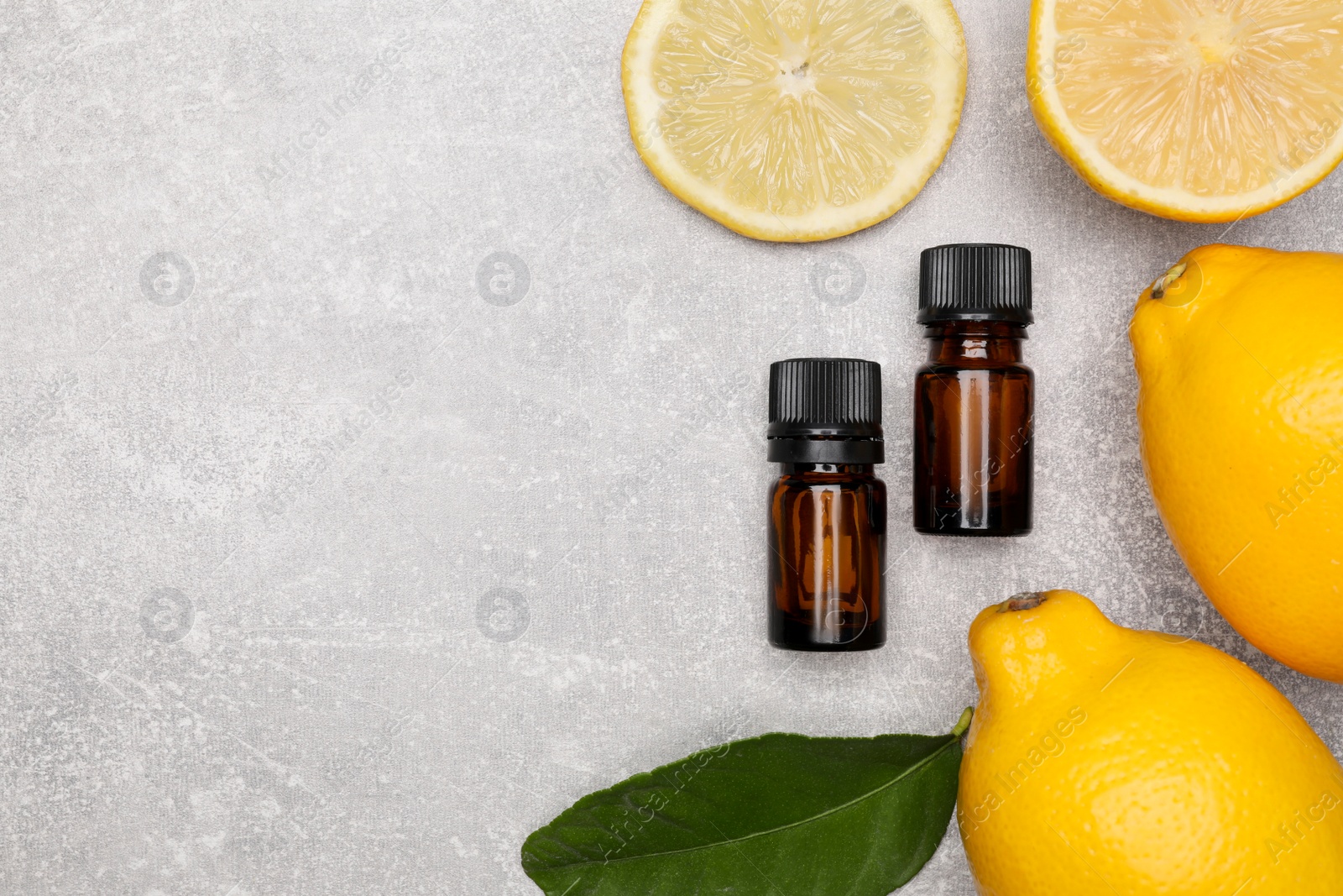 Photo of Bottles of essential oil with lemons and leaf on grey table, flat lay. Space for text