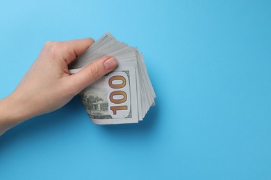 Photo of Money exchange. Woman holding dollar banknotes on light blue background, top view. Space for text